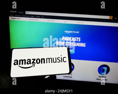 Stuttgart, Allemagne, 07-16-2022 : personne tenant un téléphone portable avec le logo du service de streaming américain Amazon Music sur l'écran devant le web d'affaires Banque D'Images