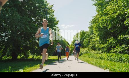 Portrait d'un groupe diversifié de personnes participant à un marathon et courant à travers un sentier de parc. Joggeurs en compétition décontractée pour la première place sur une course amicale Banque D'Images