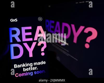 Stuttgart, Allemagne, 09-09-2022 : personne tenant un smartphone avec le site Web et le logo de la société singapourienne GXS Bank Pte. Ltd sur l'écran avec moniteur. Banque D'Images