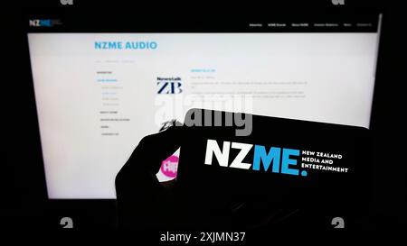 Téléphone portable avec le logo de la société New Zealand Media and Entertainment (NZME) sur l'écran en face de la page Web. Concentrez-vous sur l'affichage du téléphone Banque D'Images