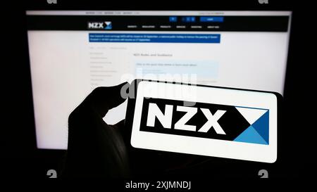 Stuttgart, Allemagne, 09-18-2022 : personne tenant un téléphone portable avec le logo de la société financière New Zealand's Exchange (NZX) sur l'écran en face de la page Web. Banque D'Images