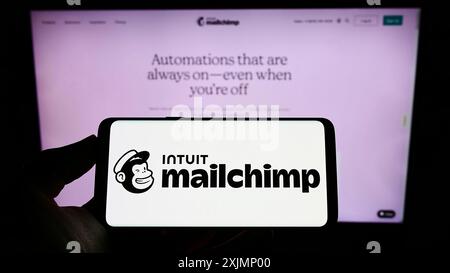 Stuttgart, Allemagne, 09-24-2022 : personne tenant un téléphone portable avec le logo de la plate-forme d'automatisation marketing Mailchimp sur l'écran devant le web d'affaires Banque D'Images