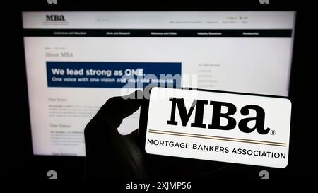 Stuttgart, Allemagne, 09-25-2022, personne tenant un téléphone portable avec le logo de l'organisation Mortgage Bankers Association (MBA) sur l'écran en face de la page Web. Banque D'Images