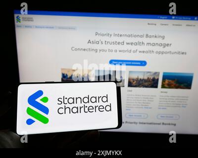 Stuttgart, Allemagne, 01-07-2023 : personne tenant un téléphone portable avec le logo de la société financière Standard Chartered plc sur l'écran devant l'entreprise Banque D'Images