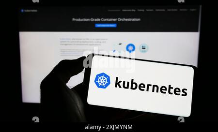 Stuttgart, Allemagne, 01-07-2023 : personne tenant un téléphone portable avec le logo du système d'orchestration de conteneur Kubernetes sur l'écran en face de la page Web. Mise au point Banque D'Images