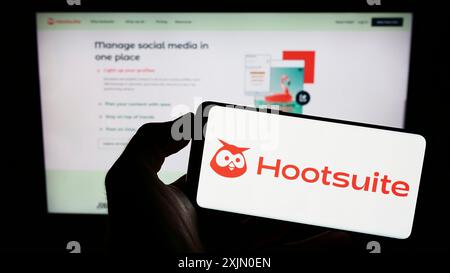 Stuttgart, Allemagne, 01-13-2023 : personne tenant un téléphone portable avec le logo de la société canadienne de logiciels Hootsuite Inc. sur l'écran devant l'entreprise Banque D'Images