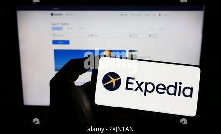 Stuttgart, Allemagne, 01-12-2023 : personne tenant un téléphone portable avec le logo de l'entreprise de l'agence de voyage en ligne Expedia sur l'écran en face de la page Web de l'entreprise. Banque D'Images