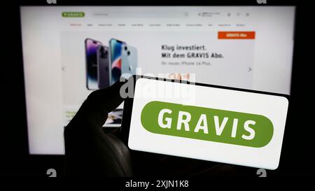 Stuttgart, Allemagne, 01-21-2023 : personne tenant un téléphone portable avec le logo de Gravis Computervertriebsgesellschaft mbH sur l'écran devant la page web. Mise au point Banque D'Images