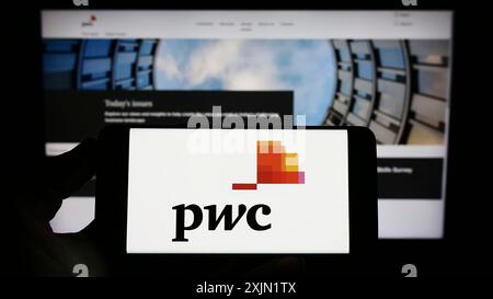 Stuttgart, Allemagne, 01-25-2023, personne tenant un téléphone portable avec le logo de la société de conseil PricewaterhouseCoopers (PWC) sur l'écran en face de la page web. Banque D'Images