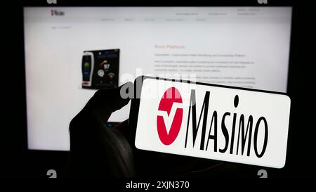 Stuttgart, Allemagne, 03-14-2023 : personne tenant un téléphone portable avec le logo de la société de technologie médicale Masimo Corporation sur l'écran en face de la page Web. Banque D'Images