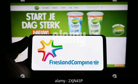 Stuttgart, Allemagne, 03-25-2023, personne tenant un smartphone avec le logo de la société Koninklijke FrieslandCampina N.V. sur l'écran devant le site. Mise au point Banque D'Images