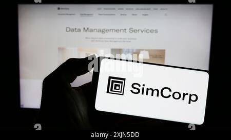 Stuttgart, Allemagne, 04 28 2023 : personne tenant un smartphone avec le logo de la société danoise de logiciels financiers SimCorp AS sur l'écran devant le site Web. Banque D'Images