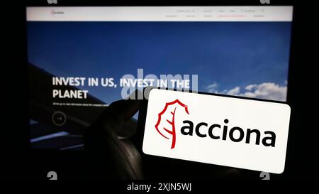 Stuttgart, Allemagne, 04-16-2023 : personne tenant un smartphone avec le logo de la société espagnole d'infrastructure Acciona S.A. sur l'écran devant le site. Banque D'Images