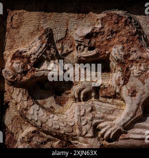 Dragon écailleux, bouche ouverte en grand et lion avec dents et griffes dénudées. Frise médiévale en ruine dans le porphyre rouge de Véronèse, Chiesa di Sant’Apollinare à trente, Trentin-Haut-Adige, Italie. Banque D'Images