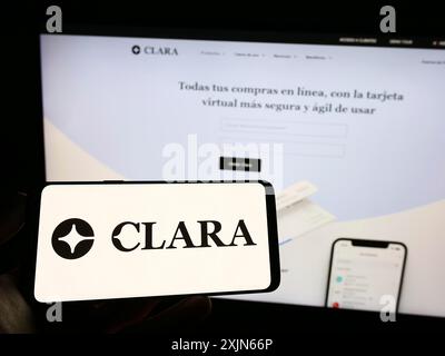 Stuttgart, Allemagne, 03-25-2023, personne tenant un téléphone portable avec le logo de la société mexicaine de fintech Clara sur l'écran en face de la page Web de l'entreprise. Concentrez-vous sur Banque D'Images