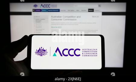 Stuttgart, Allemagne, 03 25 2023 : personne tenant un smartphone avec le logo de la Commission australienne de la concurrence et de la consommation sur l'écran devant le site Web. Banque D'Images