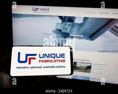 Stuttgart, Allemagne, 03-19-2023 : personne tenant un téléphone portable avec le logo de la société de fabrication américaine unique Fabricating Inc sur l'écran en face de la page Web. Banque D'Images