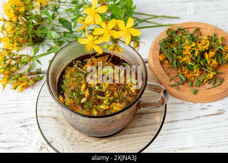 Hypericum perforatum communément appelé millepertuis, millepertuis perforés ou tisane commune au millepertuis en verre sur planche de bois blanc. Banque D'Images