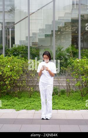 Jeune femme thaïlandaise souriant à l'extérieur en utilisant le concept de téléphone portable Banque D'Images