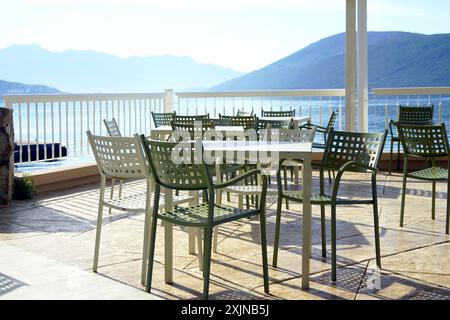 Tables et chaises vides sur une terrasse avec une vue pittoresque sur la mer et les montagnes - tôt le matin dans une ville balnéaire (Herceg Novi, Monténégro). Banque D'Images