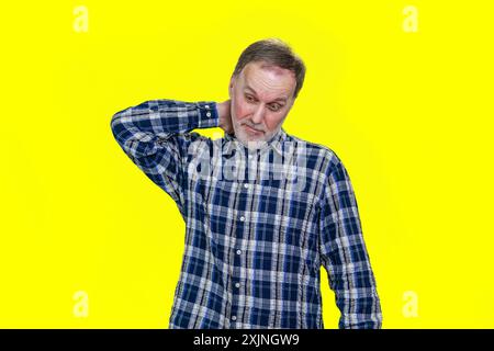 Un homme caucasien mature touche son cou. Homme habillé décontracté ayant un cache-cou debout isolé sur fond jaune. Banque D'Images