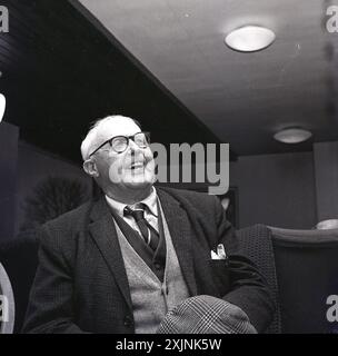 Années 1960, historique, à l'intérieur d'une maison de vieux peuples, portrait d'un homme âgé du nord, portant une veste de sport, chemise et cravate, plus deux cardigans, souriant, une vie bien vécue, Angleterre, Royaume-Uni, tenant sa casquette plate. Banque D'Images