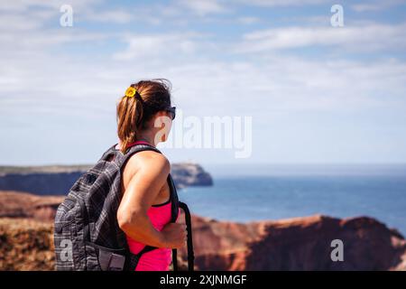 Femme mature sportive profitant de la vue de la falaise à la mer pendant la randonnée sur le sentier de trekking le long de la côte de l'Algarve au Portugal. Vacances d'été actives Banque D'Images