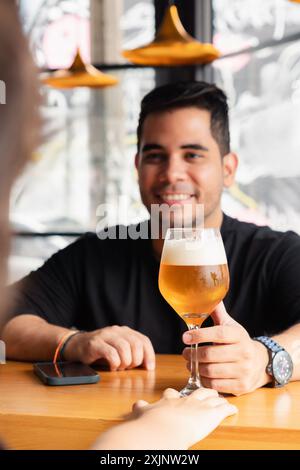 Focus sélectif sur un verre de bière lager avec un homme latino souriant en arrière-plan recevant la boisson au comptoir du bar. Le cadre est un b moderne Banque D'Images