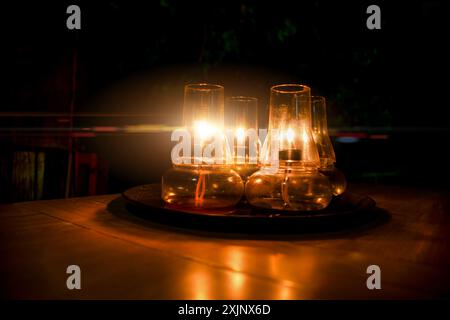 lampe à trois kérosène paraffine en verre allumée sur une table, lueur orange, paillettes de flamme Banque D'Images