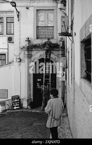 Monochrome de deux militaires à Alfama, l'un tient une échelle tandis que l'autre dégage les plantes sauvages d'une ancienne entrée envahie par la végétation Banque D'Images