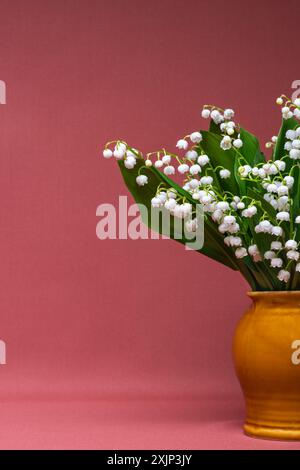 bouquet de lis blancs de la vallée dans un vase isolé sur un fond bordeaux. Rogné. Beaucoup d'espace pour le texte. Vue rapprochée de natures mortes délicates Banque D'Images