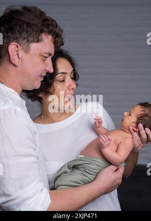 Famille heureuse avec un nouveau-né. Une mère et un père amoureux tiennent doucement leur bébé fils dans leurs bras et regardent tendrement l'enfant. Banque D'Images