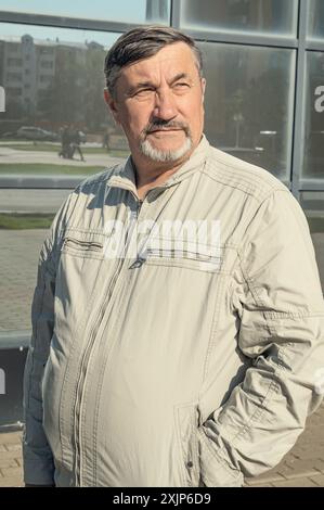 Un homme attrayant, jeune, aux cheveux gris de 70 ans avec pour toile de fond des immeubles de bureaux en verre miroir. Portrait d'une personne âgée aux cheveux gris M. Banque D'Images