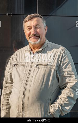 Un homme attrayant, jeune, aux cheveux gris de 70 ans avec pour toile de fond des immeubles de bureaux en verre miroir. Portrait d'une personne âgée aux cheveux gris M. Banque D'Images