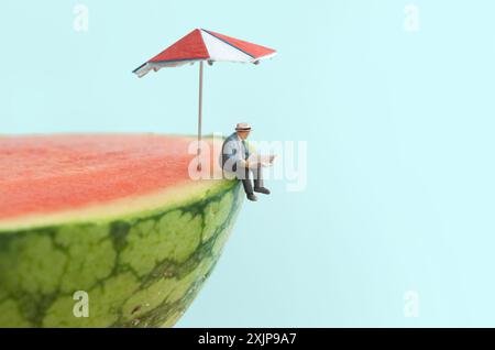 Homme d'affaires miniature lisant le journal était assis au-dessus d'une pastèque avec parasol Banque D'Images