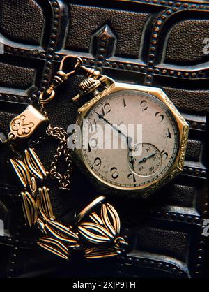 Une montre de poche en or vintage avec une chaîne délicate repose sur une surface en cuir marron foncé richement texturé. Le cadran de la montre comporte des chiffres romains et un Banque D'Images