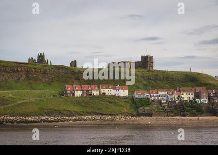 Une vue panoramique sur Whitby Abbey et les bâtiments environnants sur une colline herbeuse surplombant l'eau. Banque D'Images