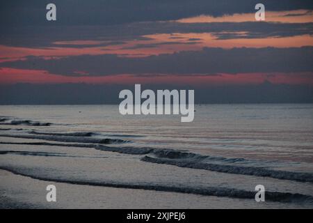 Une scène de plage tranquille au crépuscule avec des vagues douces et un ciel de coucher de soleil coloré. Banque D'Images