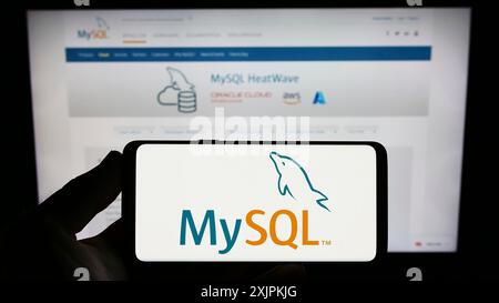 Stuttgart, Allemagne, 07-13-2023 : personne tenant un smartphone avec le logo du système de gestion de base de données relationnelle MySQL sur l'écran devant le site Web. Banque D'Images