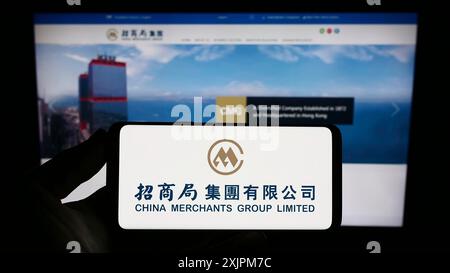 Stuttgart, Allemagne, 07-21-07 2023 : personne tenant un smartphone avec le logo de la compagnie maritime China Merchants Group Limited sur l'écran devant le site Web. Banque D'Images