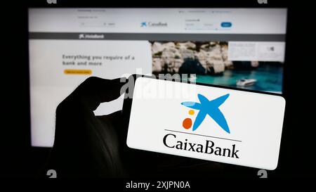 Stuttgart, Allemagne, 07-30-2023, personne tenant un smartphone avec le logo de la société financière espagnole CaixaBank S.A. sur l'écran en face du site. Mise au point Banque D'Images