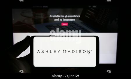 Stuttgart, Allemagne, 08-18-2023 : personne tenant un smartphone avec le logo de la société de rencontres en ligne The Ashley Madison Agency sur l'écran en face du site. Banque D'Images