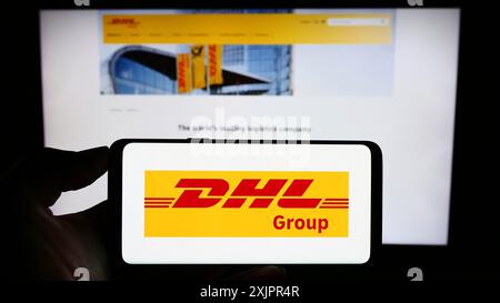 Stuttgart, Allemagne, 08-20-08 2023 : personne tenant un smartphone avec le logo de la société de logistique Deutsche Post AG (DHL Group) sur l'écran devant le site Web. Banque D'Images