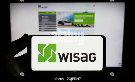 Stuttgart, Allemagne, 08-28-2023, personne tenant un smartphone avec le logo de la société allemande WISAG Dienstleistungsholding se sur l'écran devant le site web. Banque D'Images