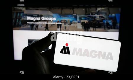 Stuttgart, Allemagne, 08 29 2023 : personne tenant un smartphone avec le logo de la société automobile Magna International Inc sur l'écran devant le site. Banque D'Images