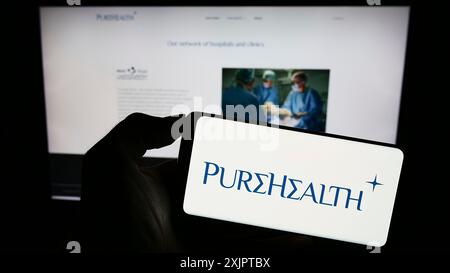 Stuttgart, Allemagne, 09-08-2023 : personne tenant un téléphone portable avec le logo de la société émiratie Pure Health LLC (PureHealth) sur l'écran en face de la page Web. Banque D'Images