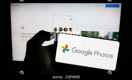 Stuttgart, Allemagne, 09-23-2023 : personne tenant un téléphone portable avec le logo de la plate-forme de stockage d'images Google photos sur l'écran en face de la page Web de l'entreprise. Banque D'Images