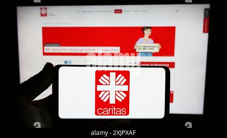 Stuttgart, Allemagne, 10-08-2023 : personne tenant un smartphone avec le logo de l'organisation allemande Deutscher Caritasverband e.V. devant le site. Mise au point Banque D'Images