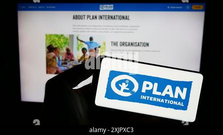 Stuttgart, Allemagne, 10-08-2023 : personne tenant un smartphone avec le logo de l'organisation de développement Plan International devant le site web. Concentrez-vous sur Banque D'Images