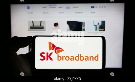 Stuttgart, Allemagne, 10-16-2023 : personne tenant un téléphone portable avec le logo de la société coréenne de télécommunications SK Broadband Inc devant l'entreprise Banque D'Images